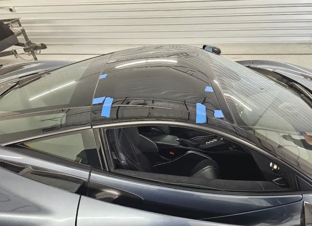 Close-up of a McLaren windshield with blue retention tape during adhesive curing after replacement