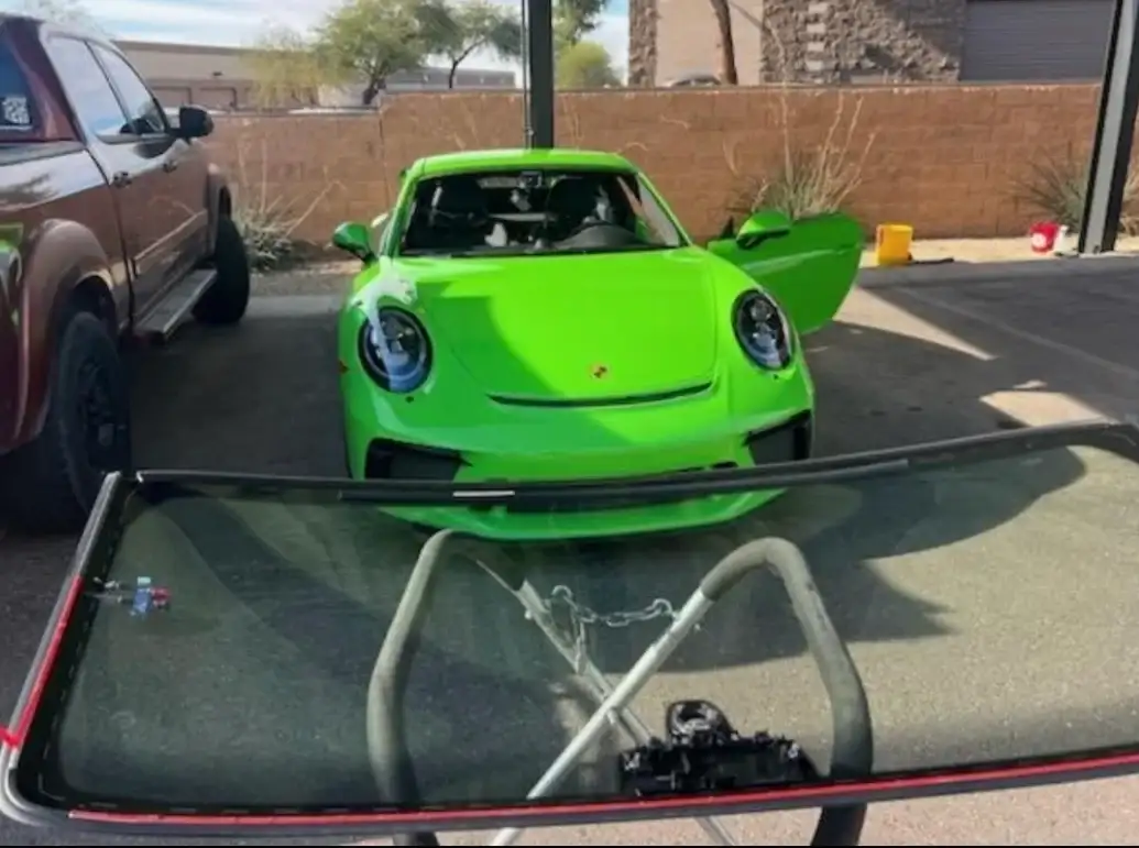 Green Porsche 911 GT3 with replacement windshield on a glass stand in the foreground at the shop