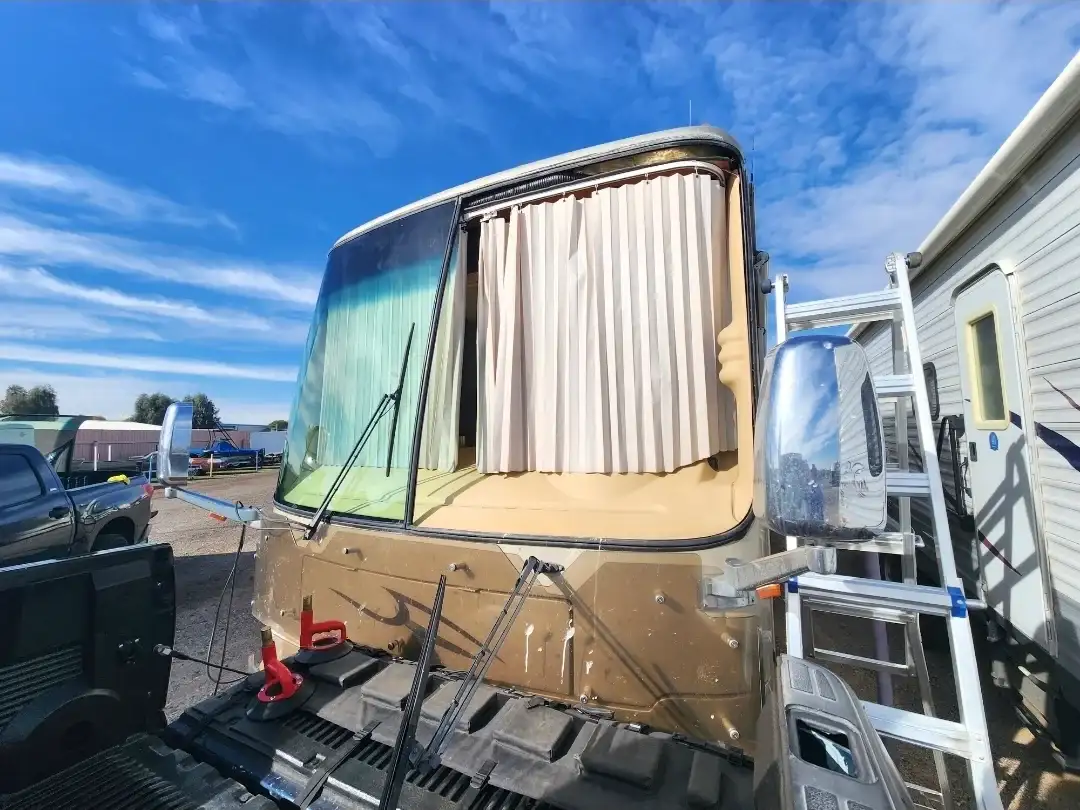 Class A motorhome windshield replacement in progress at an RV storage lot with ladder set up